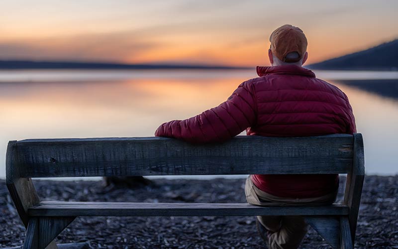 A man sits on a bench feeling unmotivated, isolated, and listless. He's frustrated he hasn't figured out how to feel better and is considering therapy.