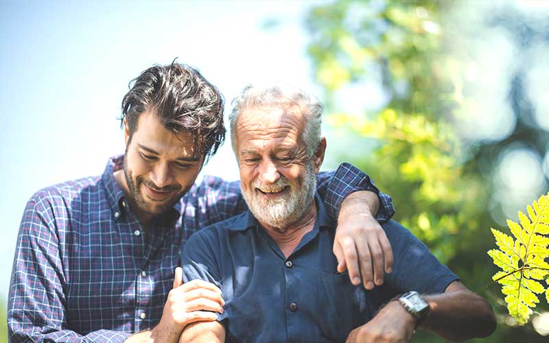 An adult father and son enjoy a moment of closeness outdoors.