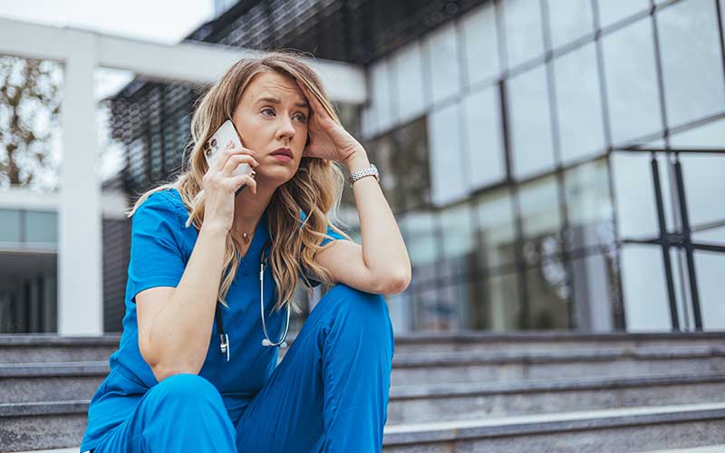 A female medical professional listens to a stressful phone conversation.