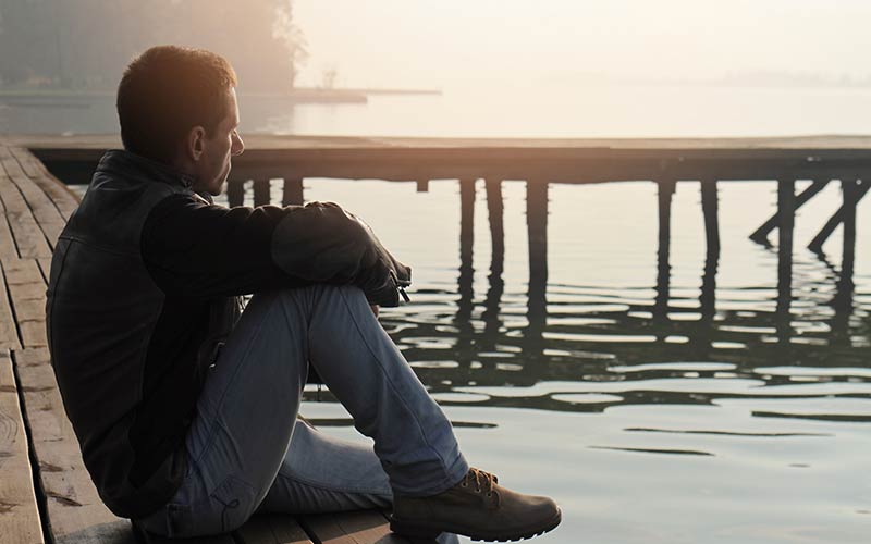 The man sitting on a dock is frustrated with life problems and thinking about doing online brief therapy for specific, targeted help and resolution.