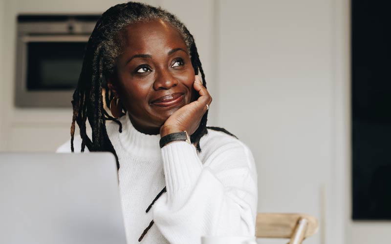 Woman sitting at table considering the progress she’s made on her problem through online brief therapy.