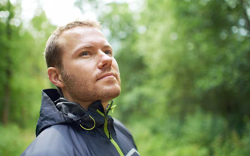 A man is enjoying a walk in the woods and starting to feel optimistic about his decreasing depression symptoms. He is starting to enjoy life again.