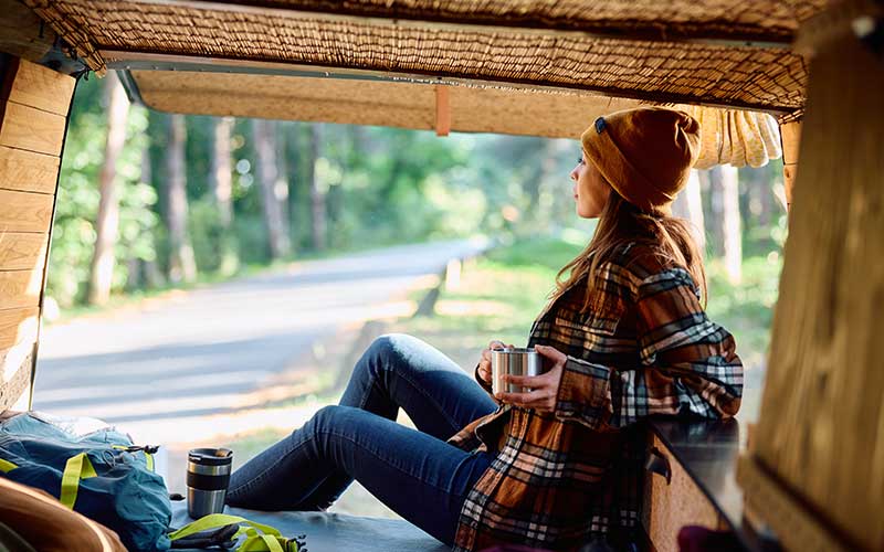 A woman enjoys coffee in the back of her camper van out in nature. She has returned to her favorite activities after starting therapy for depression.