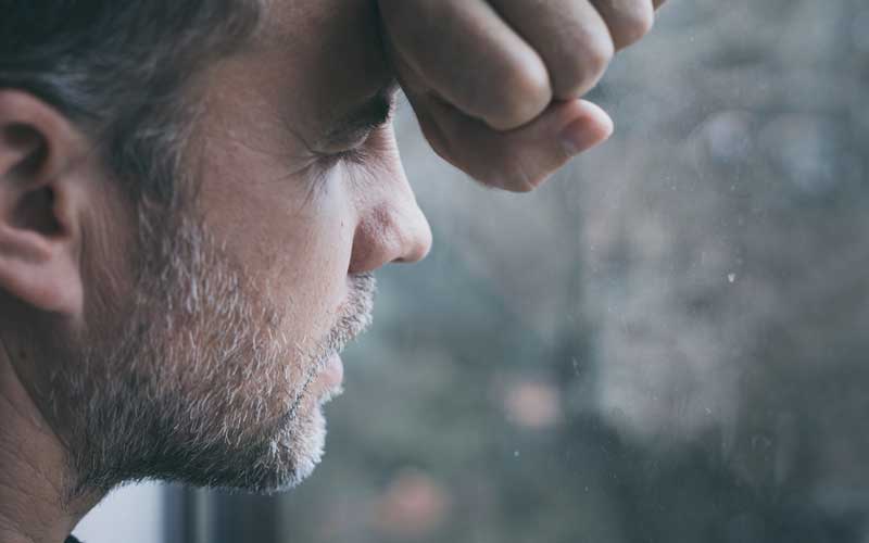 A man leans his face against a rainy window. He feels completely overwhelmed. Individual therapy with an online therapist can help with personal, professional, and relationship challenges.