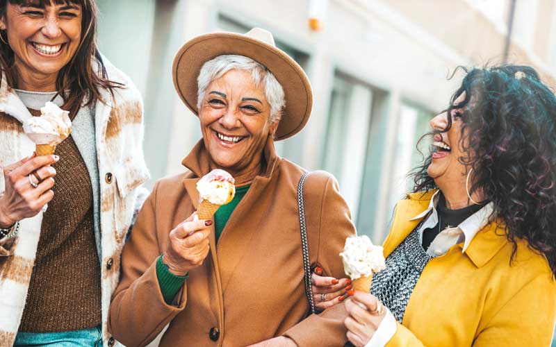 Three middle-aged women enjoy laughter and ice cream cones on a city walk. They are able to be present with each other and have a great time.